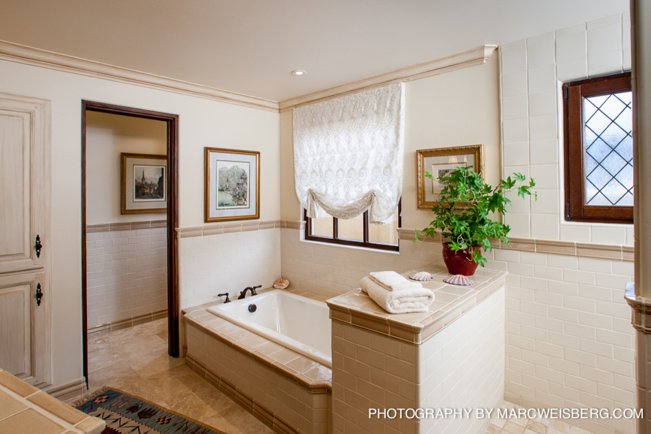 サンディエゴにある広い地中海スタイルのおしゃれなマスターバスルーム (一体型シンク、アルコーブ型シャワー、一体型トイレ	、ベージュのタイル、白い壁、ライムストーンの床、コーナー型浴槽、インセット扉のキャビネット、濃色木目調キャビネット、タイルの洗面台) の写真