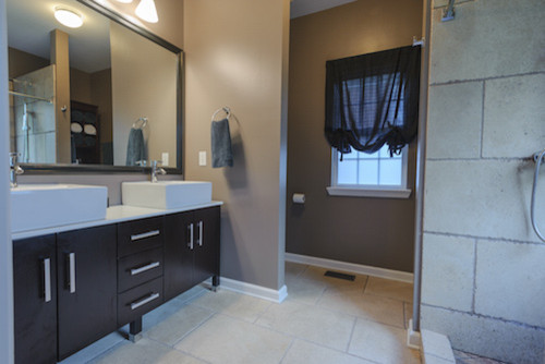 Cette image montre une salle de bain chalet avec un placard à porte plane, des portes de placard noires, un espace douche bain, WC à poser, un carrelage beige, des carreaux de céramique, un mur marron, un sol en carrelage de céramique, un plan de toilette en marbre et un sol beige.