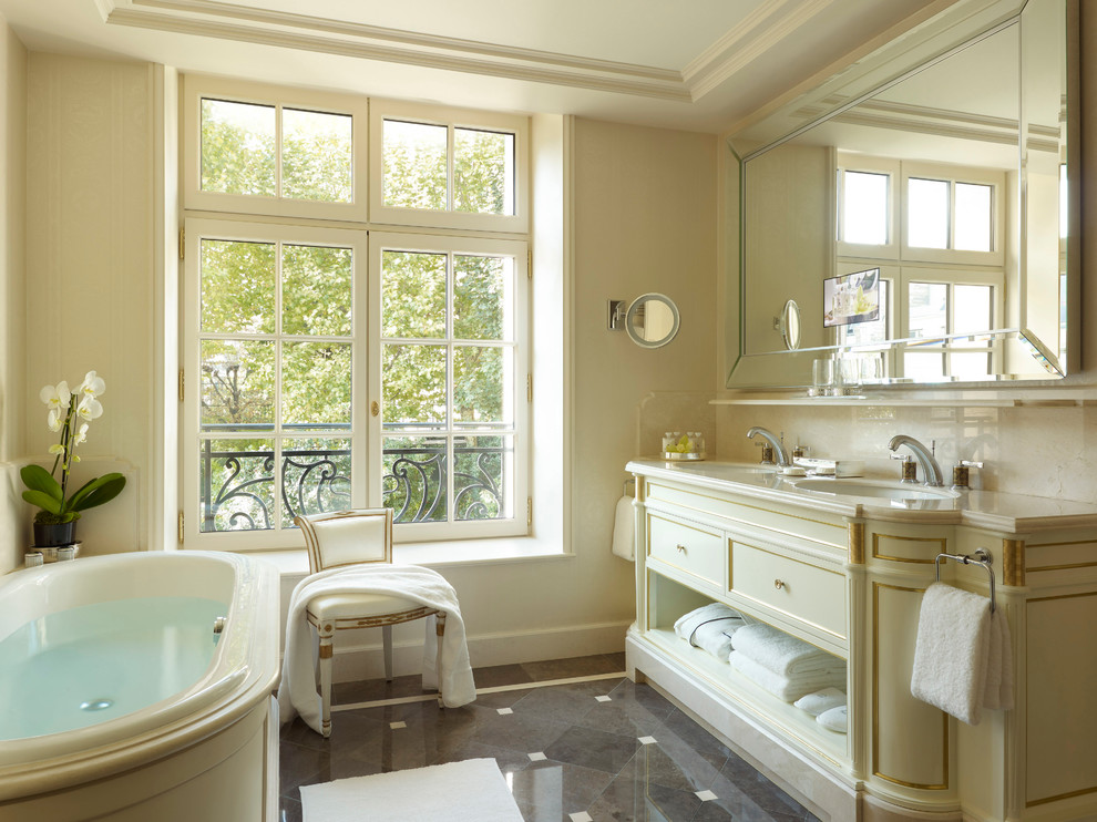 Aménagement d'une salle de bain classique avec un lavabo encastré, des portes de placard beiges, une baignoire posée et un carrelage marron.