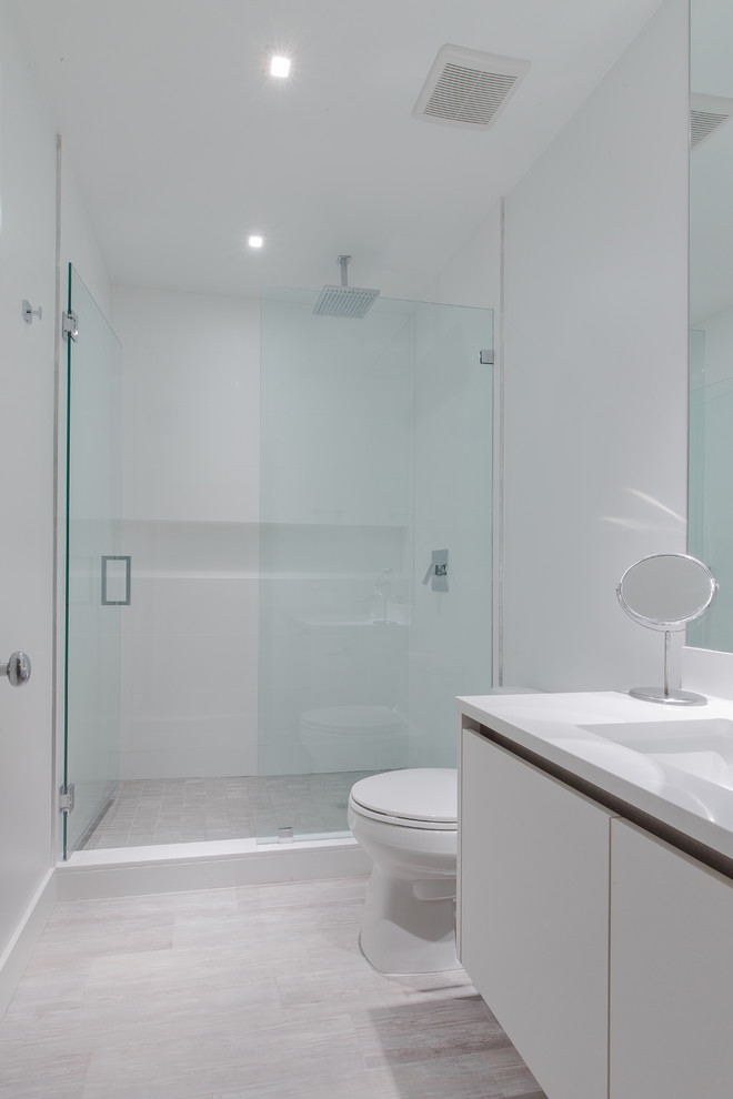 Idées déco pour une salle de bain contemporaine de taille moyenne avec un placard à porte plane, des portes de placard blanches, WC à poser, un mur blanc, parquet clair, un lavabo intégré et un plan de toilette en surface solide.