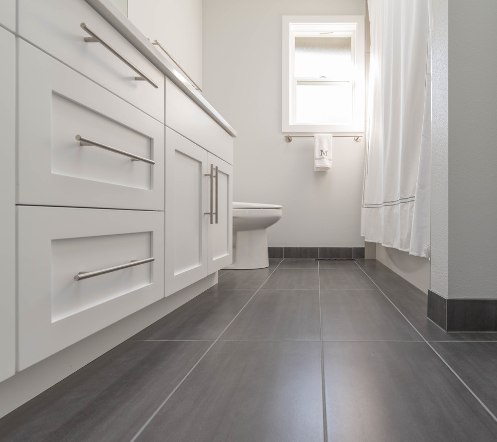 This is an example of a small modern family bathroom in Seattle with flat-panel cabinets, light wood cabinets, a built-in bath, a walk-in shower, a one-piece toilet, grey tiles, ceramic tiles, white walls, ceramic flooring, a submerged sink, engineered stone worktops and grey floors.