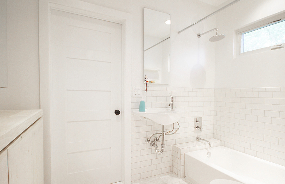 Cette image montre une salle de bain principale traditionnelle de taille moyenne avec un carrelage métro, un lavabo suspendu, une baignoire en alcôve, un combiné douche/baignoire, un carrelage blanc, un mur blanc, un sol blanc et une cabine de douche avec un rideau.