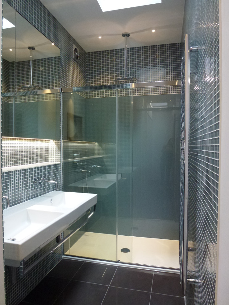 Exempel på ett mellanstort modernt vit vitt en-suite badrum, med en kantlös dusch, en vägghängd toalettstol, blå kakel, glaskakel, blå väggar, klinkergolv i keramik, ett väggmonterat handfat, svart golv och dusch med skjutdörr