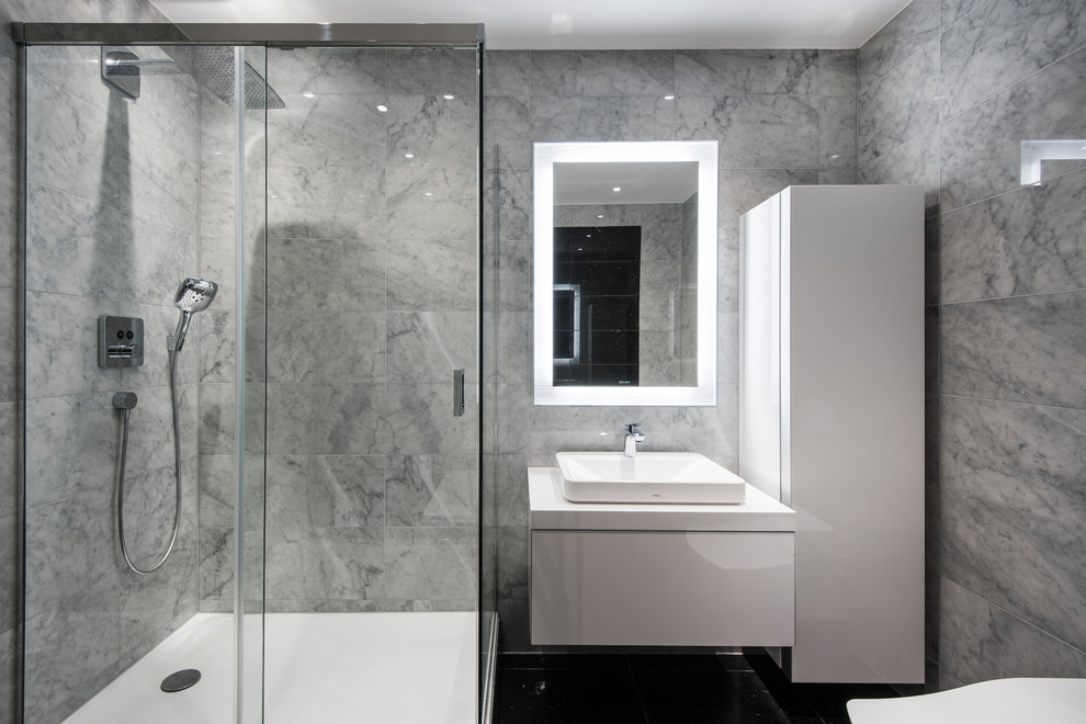 Foto på ett mellanstort funkis vit badrum för barn, med möbel-liknande, vita skåp, ett fristående badkar, en hörndusch, en vägghängd toalettstol, grå kakel, marmorkakel, grå väggar, svart golv och dusch med skjutdörr