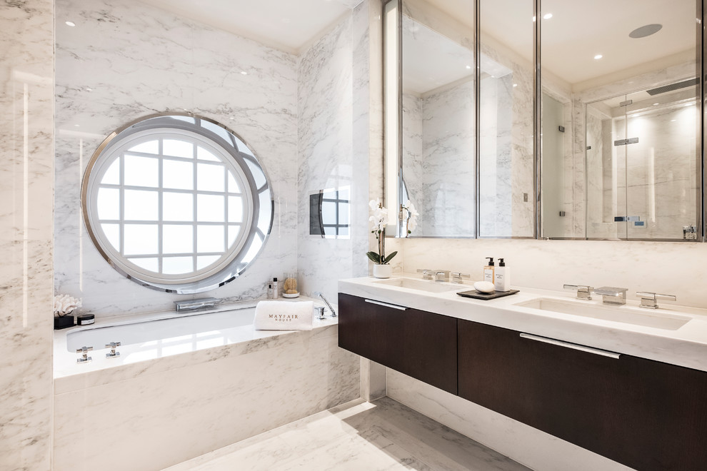 На фото: главная ванная комната в современном стиле с плоскими фасадами, белой плиткой, мраморной плиткой, белыми стенами, мраморным полом, белым полом, белой столешницей, темными деревянными фасадами, ванной в нише, врезной раковиной и мраморной столешницей