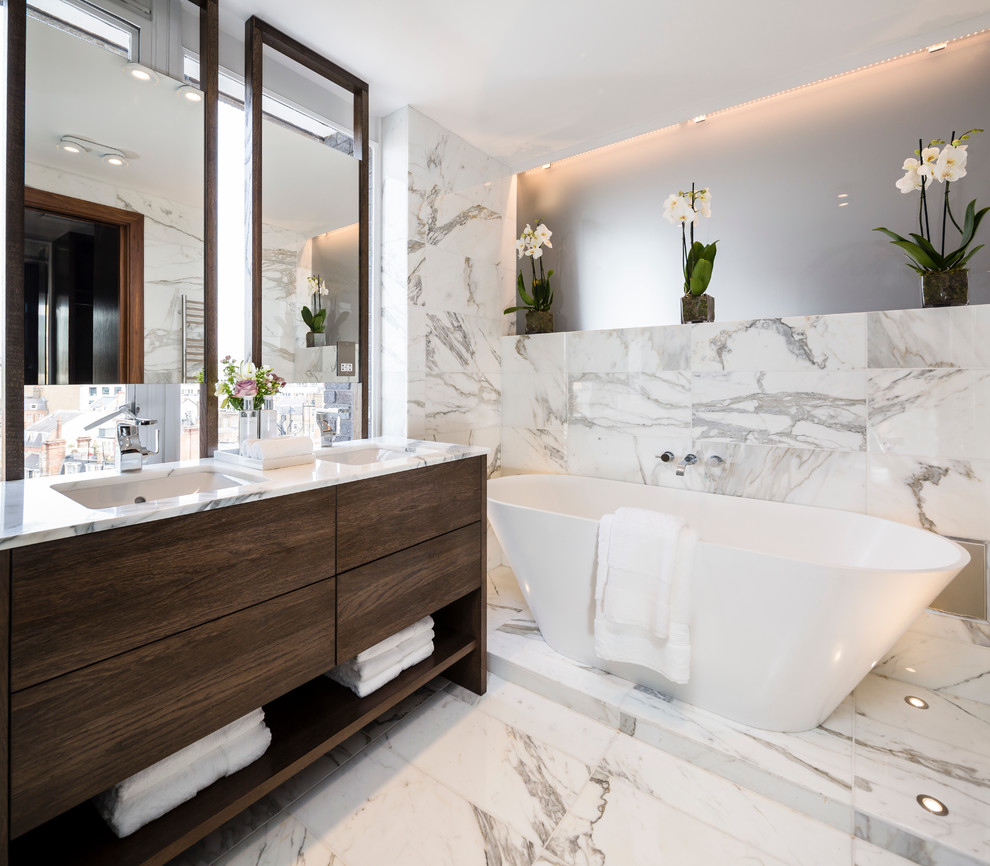 Modern inredning av ett en-suite badrum, med släta luckor, skåp i mörkt trä, ett fristående badkar, grå kakel, vit kakel, flerfärgade väggar, marmorgolv och ett undermonterad handfat