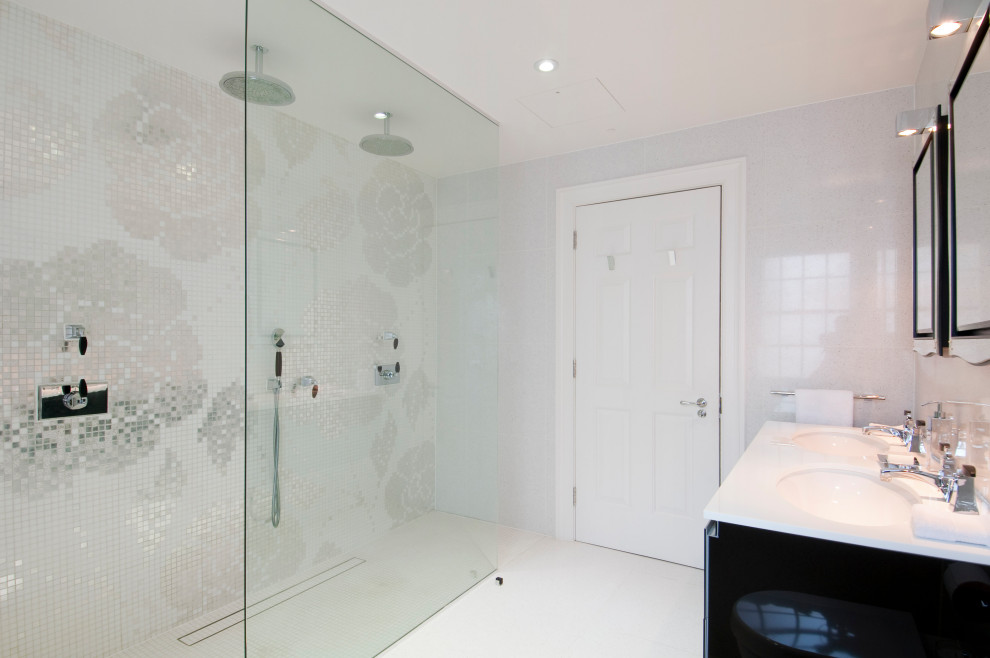 Design ideas for a medium sized contemporary ensuite bathroom in London with flat-panel cabinets, black cabinets, a submerged bath, a walk-in shower, a wall mounted toilet, white tiles, stone tiles, white walls, a submerged sink, glass worktops, white floors, an open shower, white worktops, double sinks and a floating vanity unit.