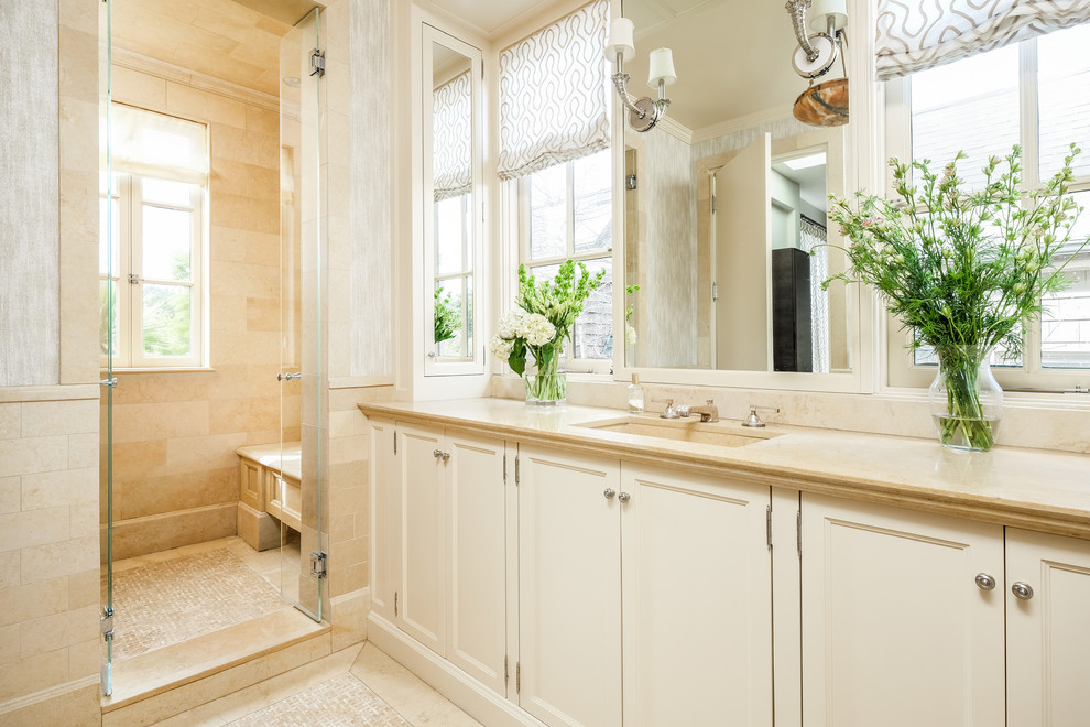 Foto på ett vintage beige badrum, med luckor med profilerade fronter, vita skåp, beige kakel, beige väggar, ett undermonterad handfat, beiget golv och dusch med gångjärnsdörr