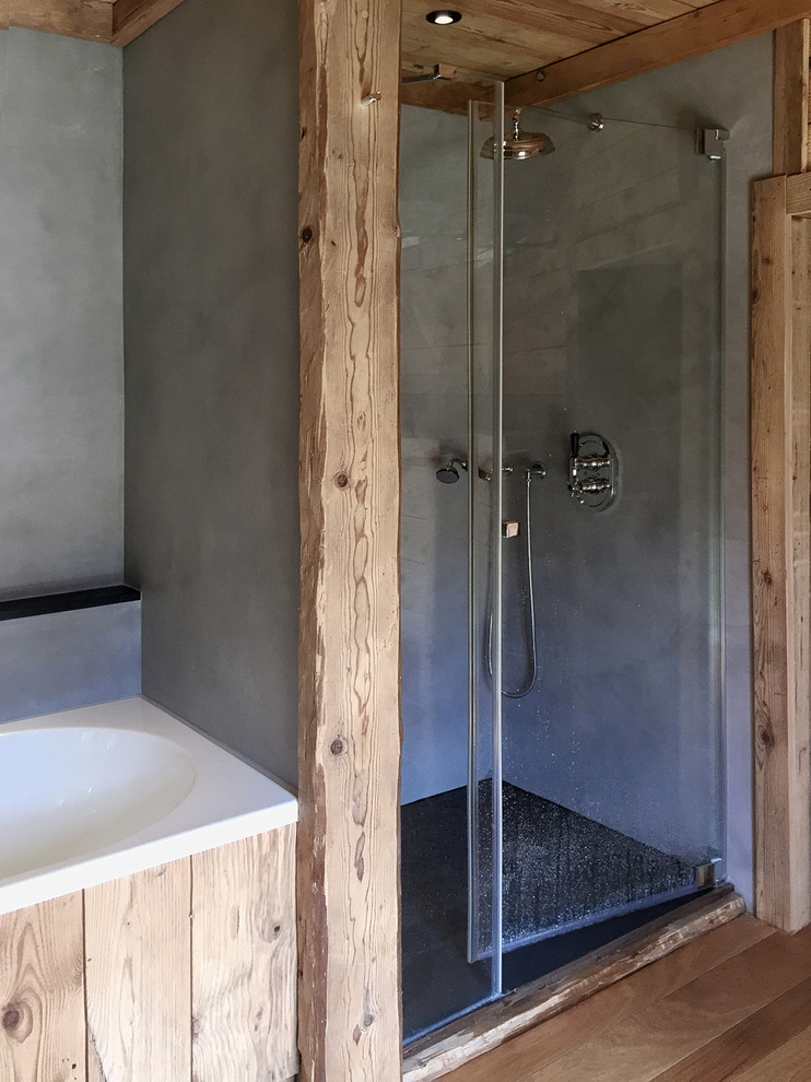 Photo of a medium sized country family bathroom in Lyon with a built-in sink, flat-panel cabinets, medium wood cabinets, solid surface worktops, an alcove bath, a walk-in shower, a wall mounted toilet, grey walls and light hardwood flooring.
