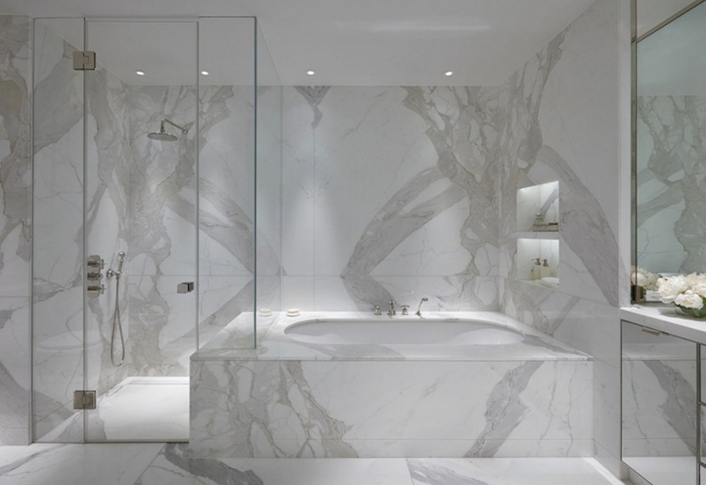 На фото: большая главная ванная комната в стиле модернизм с плоскими фасадами, полновстраиваемой ванной, душем в нише, серой плиткой, белой плиткой, мраморной плиткой, белыми стенами, мраморным полом, мраморной столешницей, белым полом, душем с распашными дверями и белой столешницей с