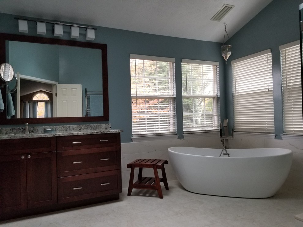 Пример оригинального дизайна: большая главная ванная комната с фасадами в стиле шейкер, коричневыми фасадами, отдельно стоящей ванной, белой плиткой, керамогранитной плиткой, синими стенами, полом из керамогранита, врезной раковиной, столешницей из гранита, белым полом и разноцветной столешницей