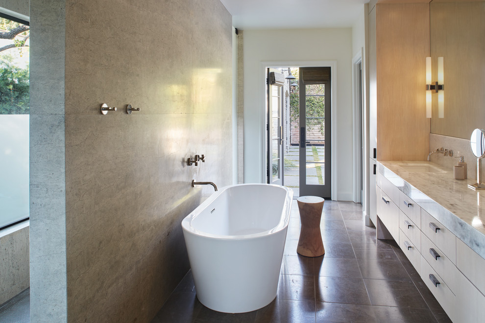 Photo of a contemporary ensuite bathroom in Los Angeles with flat-panel cabinets, beige cabinets, a freestanding bath, a built-in shower, grey tiles, stone slabs, beige walls, a submerged sink, grey floors, an open shower and grey worktops.