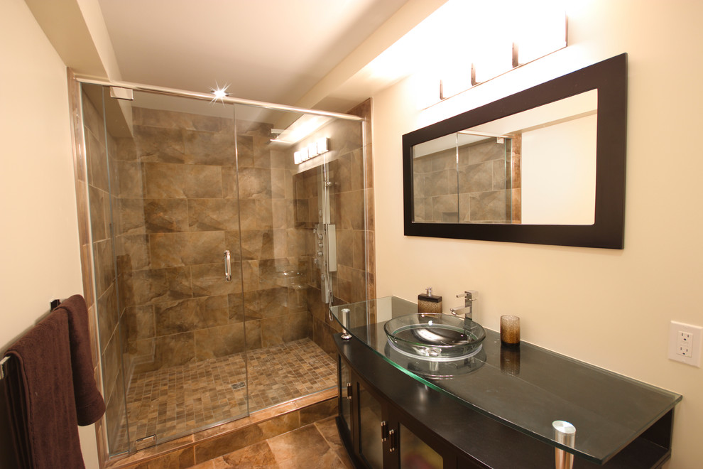 Aménagement d'une salle de bain contemporaine en bois foncé de taille moyenne avec une vasque, un placard à porte vitrée, un plan de toilette en verre, WC à poser, un carrelage marron, des carreaux de céramique, un mur beige et un sol en carrelage de céramique.