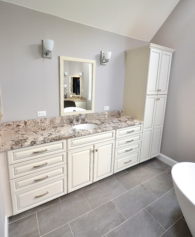 Design ideas for a large classic ensuite bathroom in Philadelphia with raised-panel cabinets, granite worktops, a freestanding bath, a one-piece toilet, porcelain tiles, grey walls, porcelain flooring, white cabinets, a corner shower, beige tiles, a submerged sink, grey floors and a hinged door.
