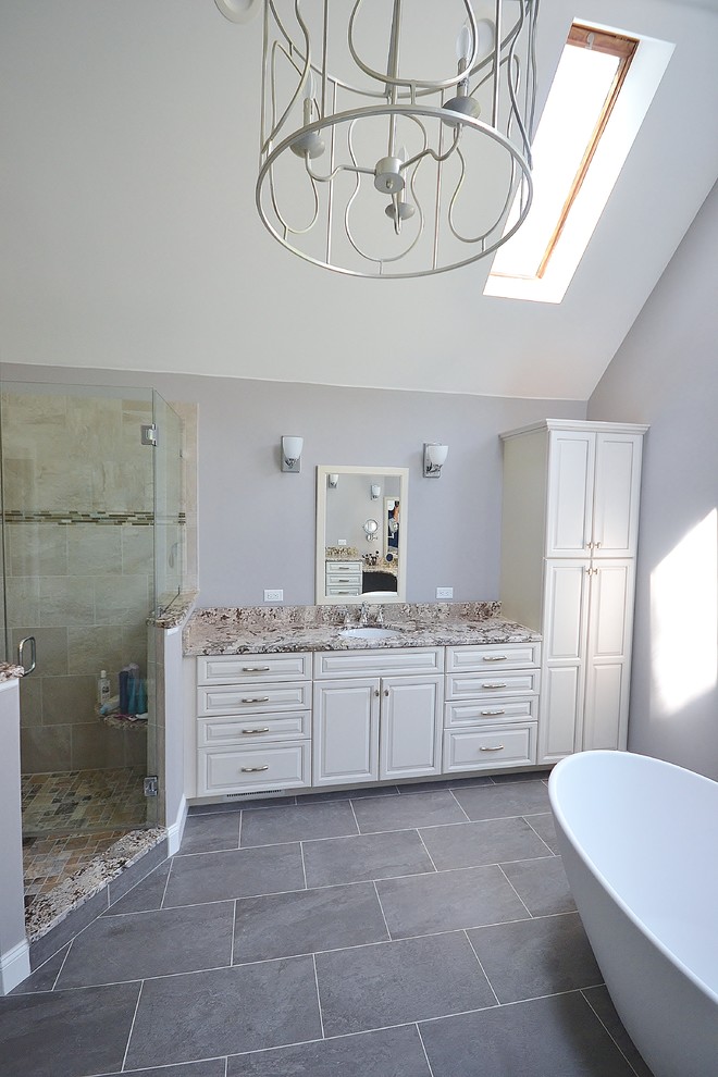 This is an example of a large traditional ensuite bathroom in Philadelphia with raised-panel cabinets, granite worktops, a freestanding bath, a one-piece toilet, porcelain tiles, grey walls, porcelain flooring, white cabinets, a corner shower, beige tiles, a submerged sink, grey floors and a hinged door.