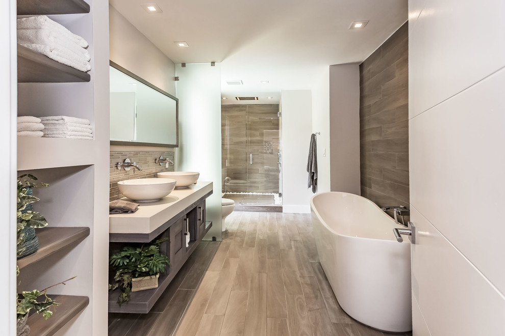 Cette image montre une douche en alcôve principale design avec des portes de placard grises, une baignoire indépendante, un carrelage gris, un mur blanc, une vasque, un sol gris, une cabine de douche à porte battante et un placard à porte shaker.