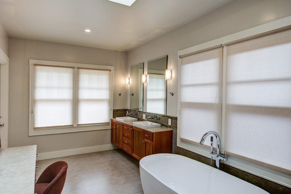 Large classic ensuite bathroom in San Francisco with a vessel sink, recessed-panel cabinets, medium wood cabinets, limestone worktops, a freestanding bath, an alcove shower, a wall mounted toilet, brown tiles, glass tiles, grey walls and porcelain flooring.