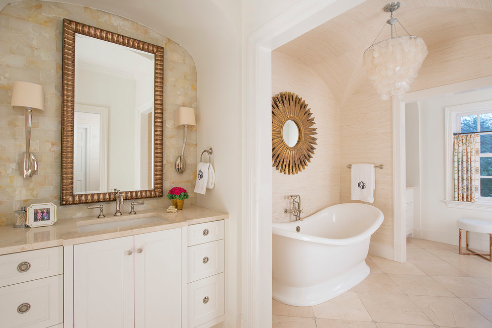 Foto på ett vintage badrum, med ett undermonterad handfat, luckor med infälld panel, vita skåp, ett fristående badkar, beige kakel, beige väggar och beiget golv