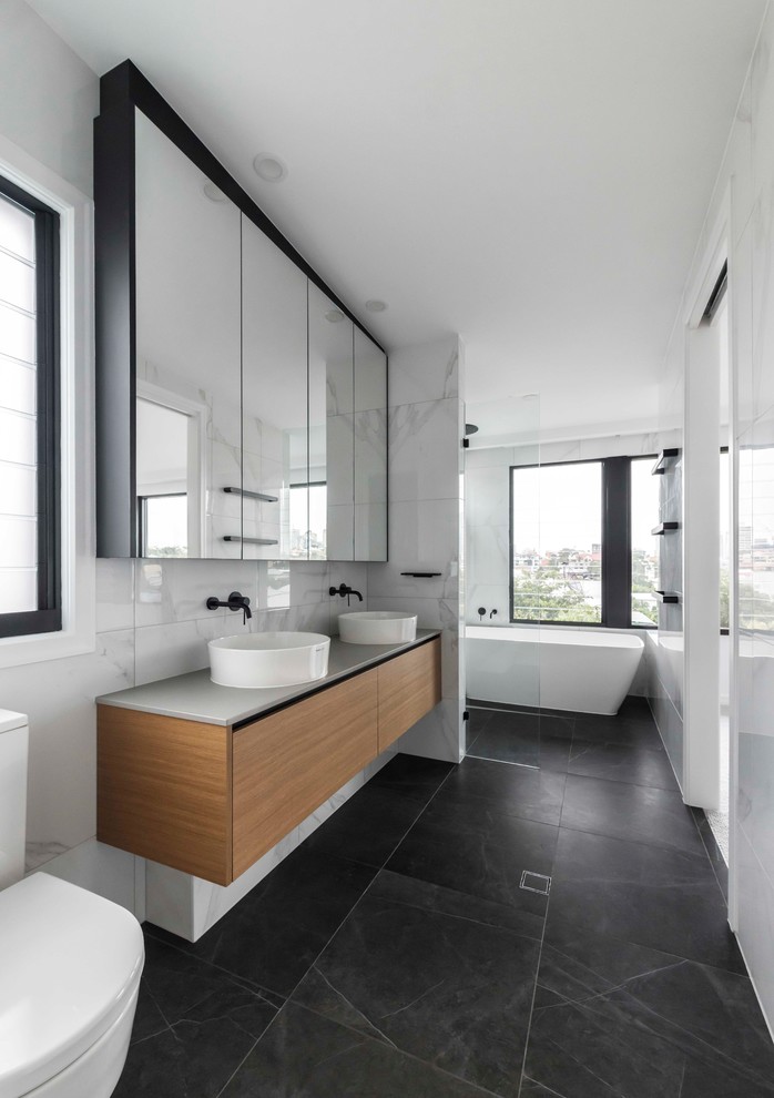 Cette image montre une salle de bain principale design en bois clair avec une baignoire indépendante, un espace douche bain, un carrelage blanc, un mur blanc, un sol en carrelage de céramique, un sol gris et un plan de toilette gris.
