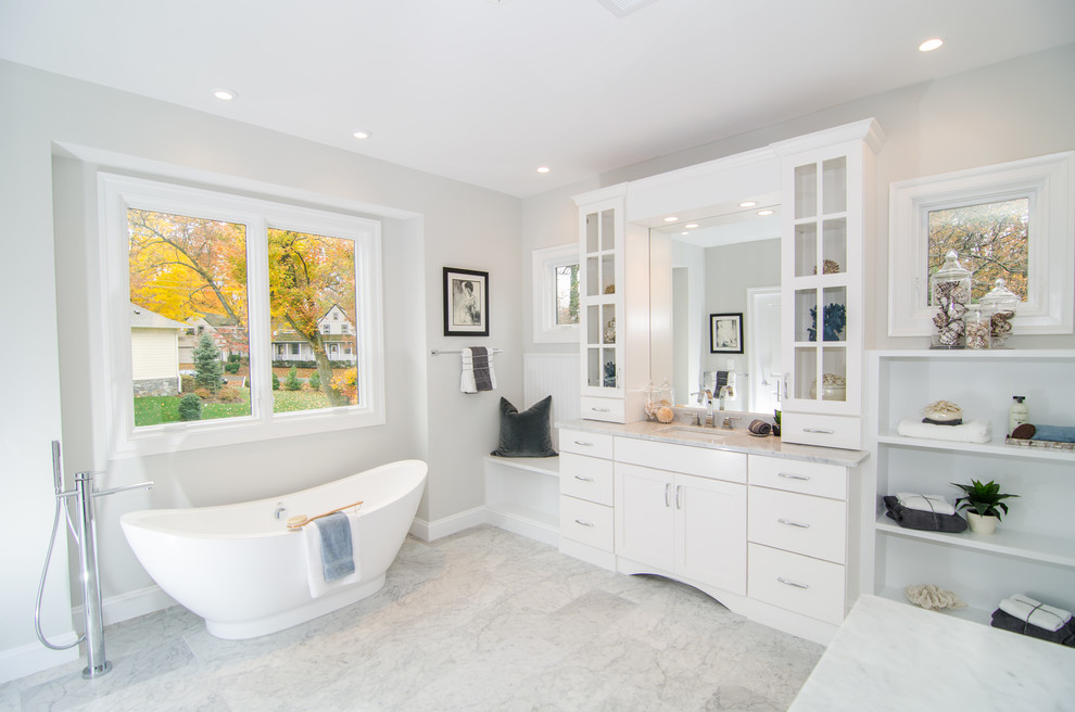 ワシントンD.C.にあるトランジショナルスタイルのおしゃれな浴室 (アンダーカウンター洗面器、フラットパネル扉のキャビネット、白いキャビネット、置き型浴槽、グレーの壁) の写真