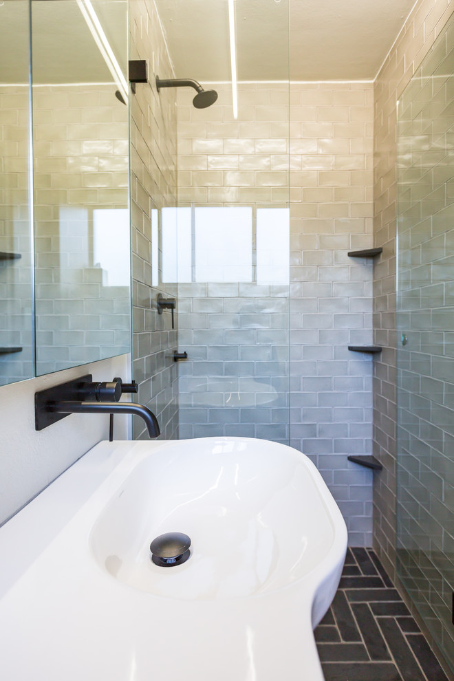 Inredning av ett modernt litet badrum med dusch, med en dusch i en alkov, en toalettstol med hel cisternkåpa, grå kakel, keramikplattor, vita väggar, skiffergolv, ett väggmonterat handfat, svart golv, med dusch som är öppen, luckor med glaspanel och skåp i ljust trä