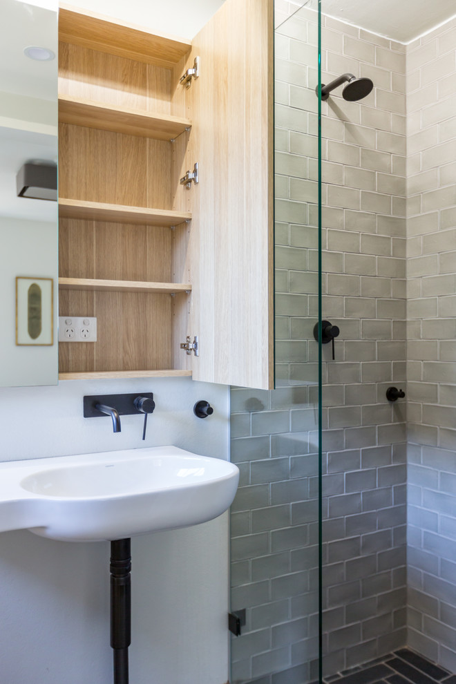 Klassisk inredning av ett litet badrum med dusch, med luckor med glaspanel, skåp i ljust trä, en dusch i en alkov, en toalettstol med hel cisternkåpa, grå kakel, keramikplattor, vita väggar, skiffergolv, ett väggmonterat handfat, svart golv och med dusch som är öppen