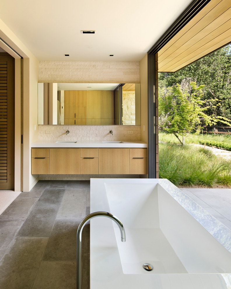 Modern inredning av ett badrum, med ett undermonterad handfat, släta luckor, skåp i mellenmörkt trä, ett fristående badkar och beige kakel