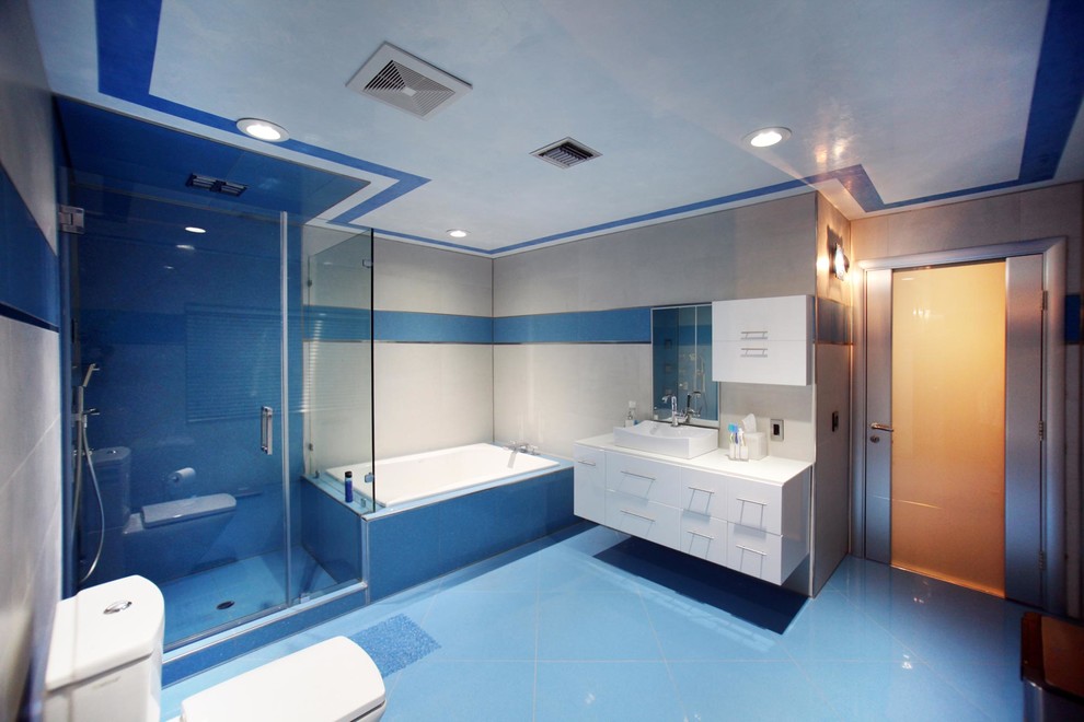 Idéer för att renovera ett stort funkis en-suite badrum, med släta luckor, vita skåp, en hörndusch, en toalettstol med separat cisternkåpa, blå kakel, grå kakel, cementkakel, grå väggar, laminatgolv, ett fristående handfat, bänkskiva i akrylsten, blått golv och ett platsbyggt badkar