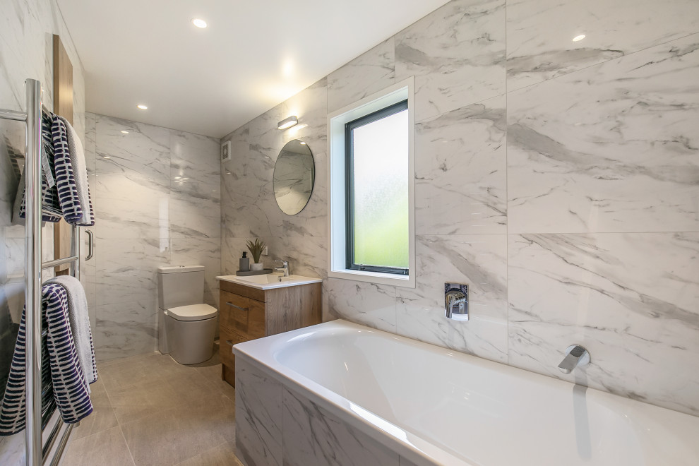 Mid-sized trendy 3/4 gray tile porcelain tile and beige floor drop-in bathtub photo in Auckland with flat-panel cabinets, medium tone wood cabinets, a two-piece toilet, an integrated sink and white countertops