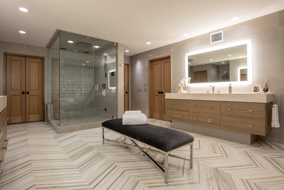 На фото: главная ванная комната в современном стиле с плоскими фасадами, фасадами цвета дерева среднего тона, угловым душем, серой плиткой, разноцветным полом, бежевой столешницей и зеркалом с подсветкой