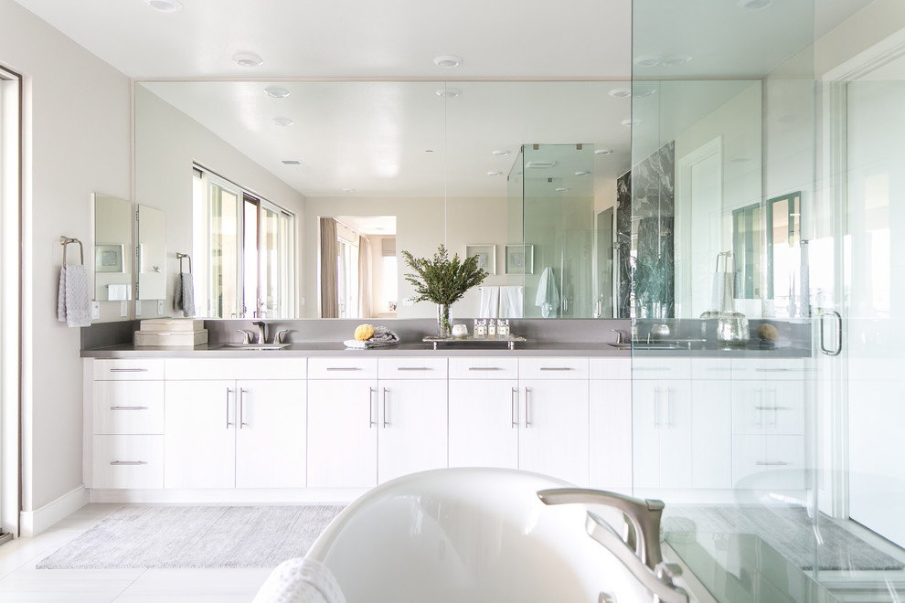 Ejemplo de cuarto de baño principal actual con puertas de armario blancas, bañera exenta, baldosas y/o azulejos de mármol, encimera de cuarcita y encimeras grises