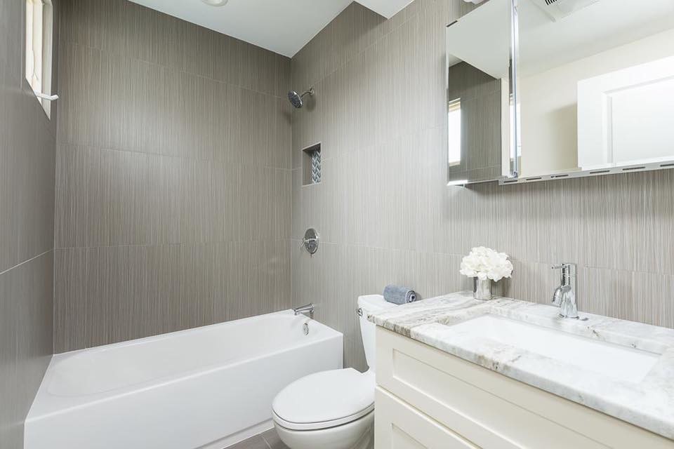 Cette image montre une petite salle de bain design pour enfant avec un placard avec porte à panneau surélevé, des portes de placard blanches, une baignoire posée, un combiné douche/baignoire, WC à poser, un carrelage blanc, des carreaux de porcelaine, un mur marron, un sol en carrelage de porcelaine, un lavabo encastré, un plan de toilette en marbre, un sol gris et une cabine de douche avec un rideau.