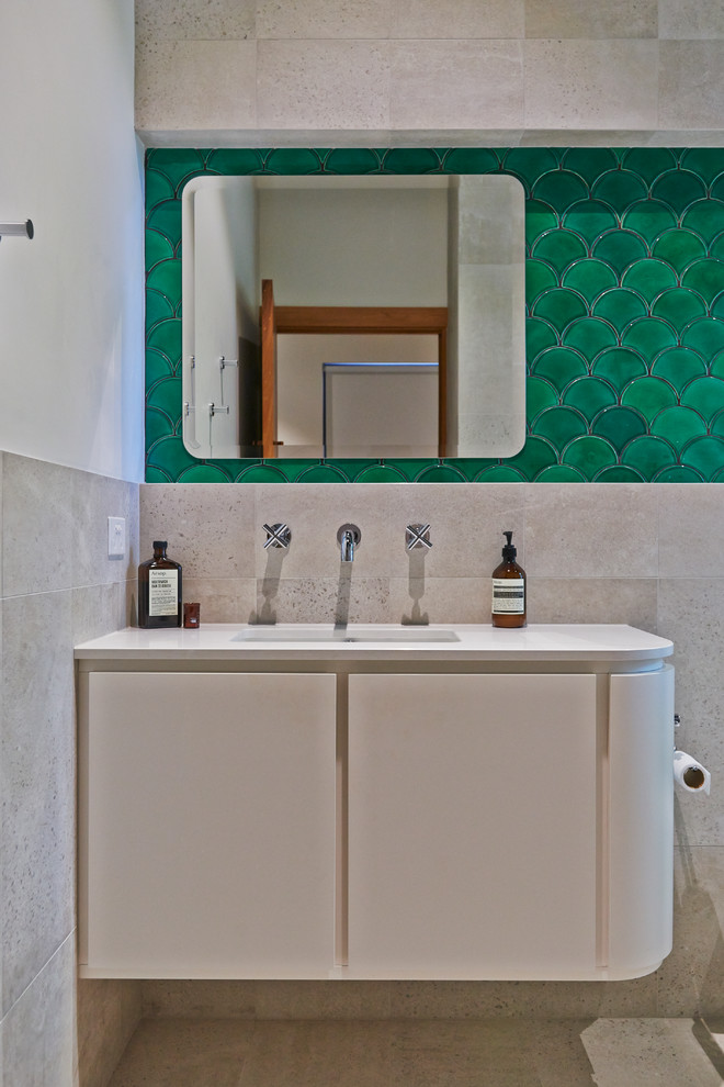 Cette photo montre une petite salle de bain éclectique avec un placard en trompe-l'oeil, des portes de placard blanches, une douche ouverte, WC suspendus, un carrelage vert, des carreaux de céramique, un mur beige, un sol en calcaire, un lavabo encastré et un plan de toilette en surface solide.