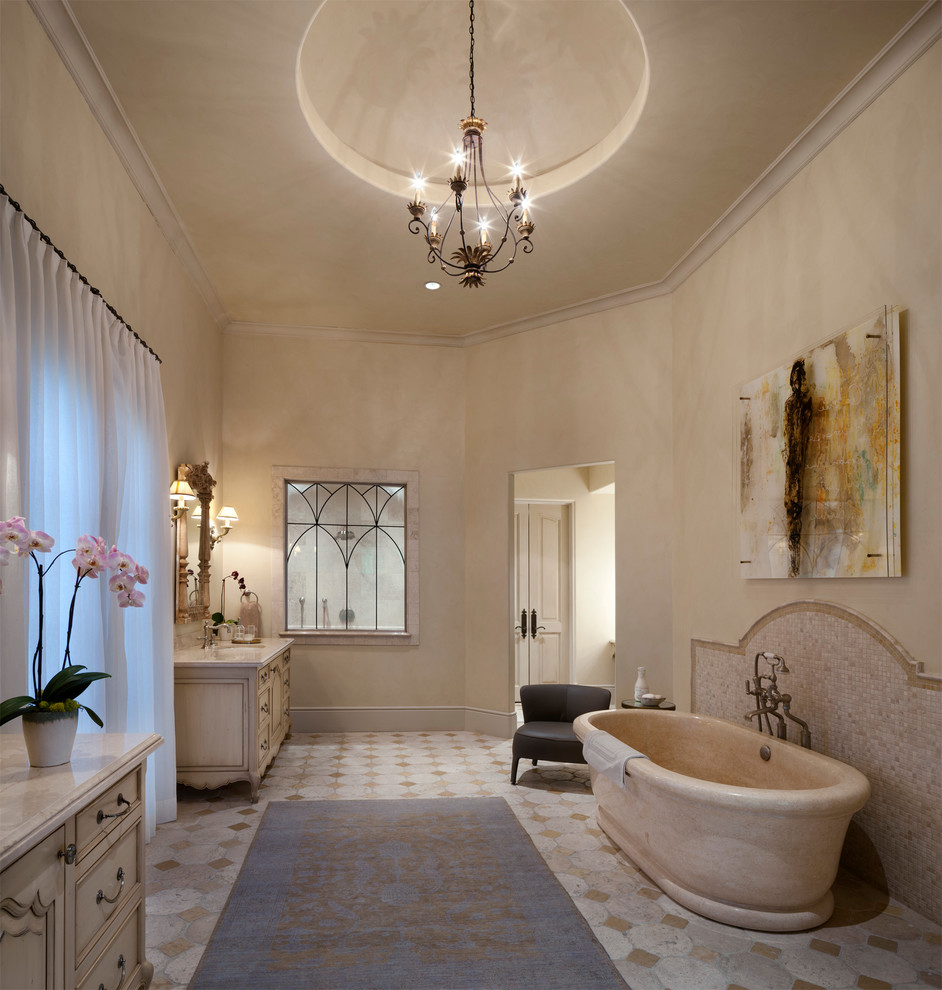 Пример оригинального дизайна: большая главная ванная комната в средиземноморском стиле с отдельно стоящей ванной, бежевыми стенами, врезной раковиной, фасадами с утопленной филенкой, светлыми деревянными фасадами, мраморной столешницей, бежевой плиткой и полом из керамической плитки