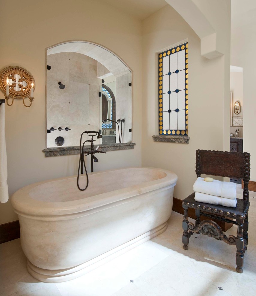 Mediterranes Badezimmer mit freistehender Badewanne, dunklen Holzschränken, Marmor-Waschbecken/Waschtisch, beigen Fliesen und Steinfliesen in Dallas