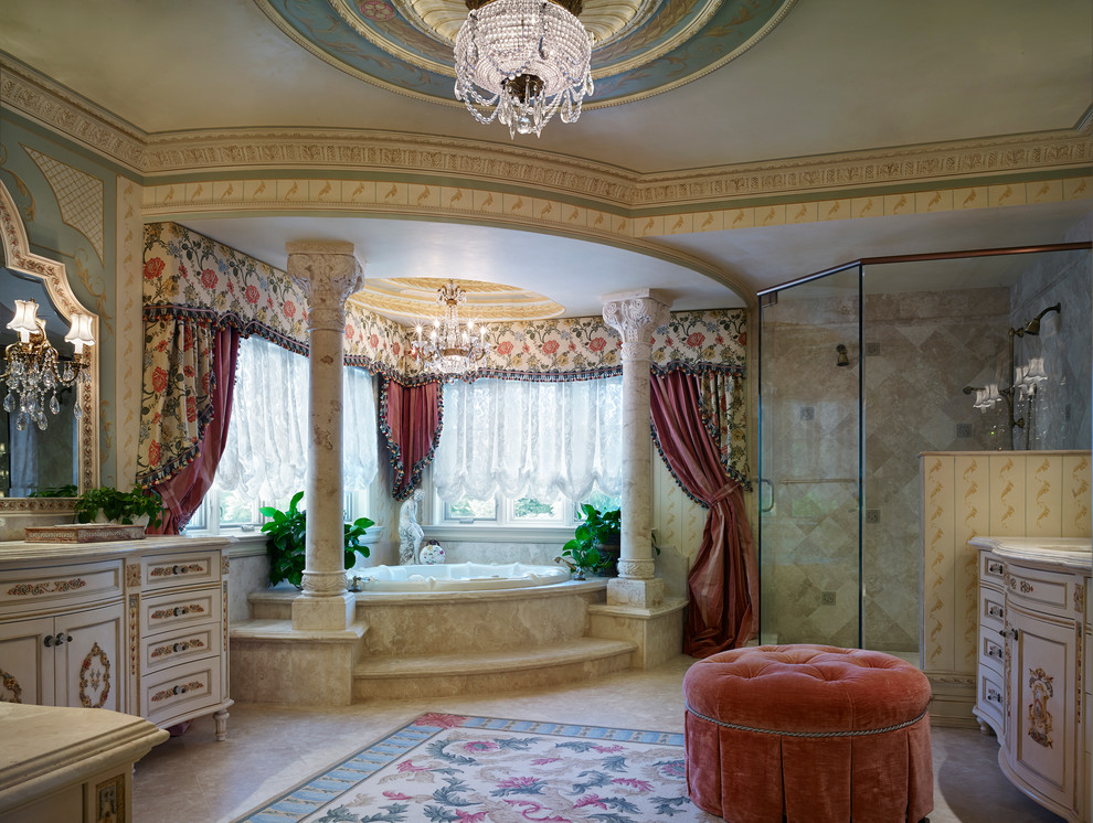 Cette image montre une grande salle de bain principale traditionnelle avec un plan de toilette en marbre, une baignoire d'angle, un carrelage beige, un mur multicolore, un lavabo encastré, un placard en trompe-l'oeil, des portes de placard beiges, une douche d'angle, un carrelage de pierre et un sol en marbre.