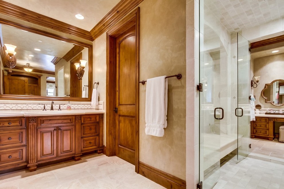 Inspiration for a large mediterranean master beige tile and stone tile limestone floor and beige floor bathroom remodel in San Diego with raised-panel cabinets, medium tone wood cabinets, a one-piece toilet, beige walls, marble countertops, an undermount sink and white countertops