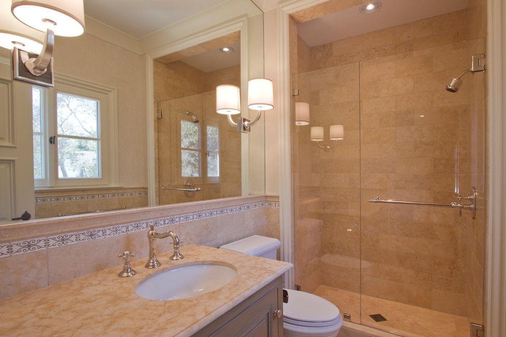 Cette photo montre une petite salle de bain méditerranéenne avec un placard à porte affleurante, des portes de placard beiges, WC à poser, un carrelage beige, un mur beige, un lavabo encastré, un plan de toilette en marbre, un carrelage de pierre et un sol en marbre.