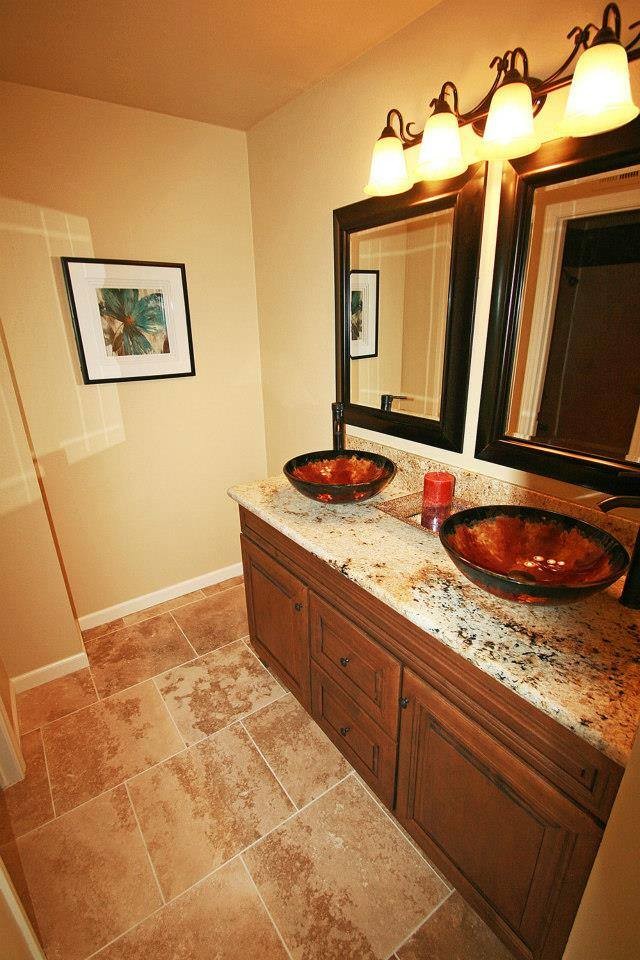 Immagine di una stanza da bagno padronale mediterranea di medie dimensioni con ante con bugna sagomata, ante in legno scuro, piastrelle beige, piastrelle in pietra, pareti gialle, pavimento in travertino, lavabo a bacinella e top in granito