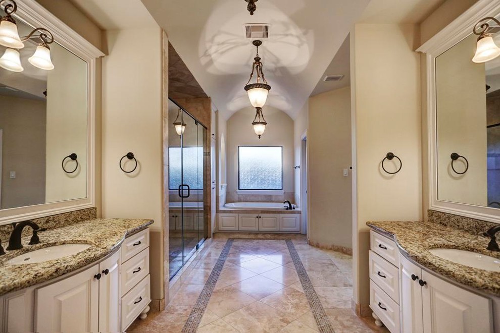 Large mediterranean ensuite bathroom in Houston with raised-panel cabinets, white cabinets, a built-in bath, a double shower, a two-piece toilet, grey tiles, travertine tiles, beige walls, travertine flooring, a submerged sink, granite worktops, beige floors, a hinged door and grey worktops.