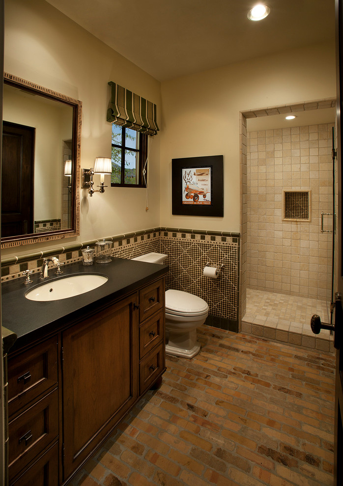 フェニックスにある中くらいな地中海スタイルのおしゃれなバスルーム (浴槽なし) (アンダーカウンター洗面器、濃色木目調キャビネット、ベージュの壁、レンガの床、アルコーブ型シャワー、分離型トイレ) の写真
