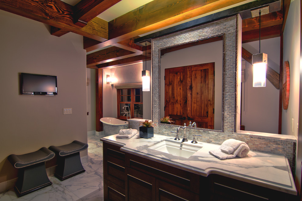 На фото: большая главная ванная комната в современном стиле с врезной раковиной, темными деревянными фасадами, отдельно стоящей ванной, синей плиткой, серыми стенами, мраморным полом и мраморной столешницей