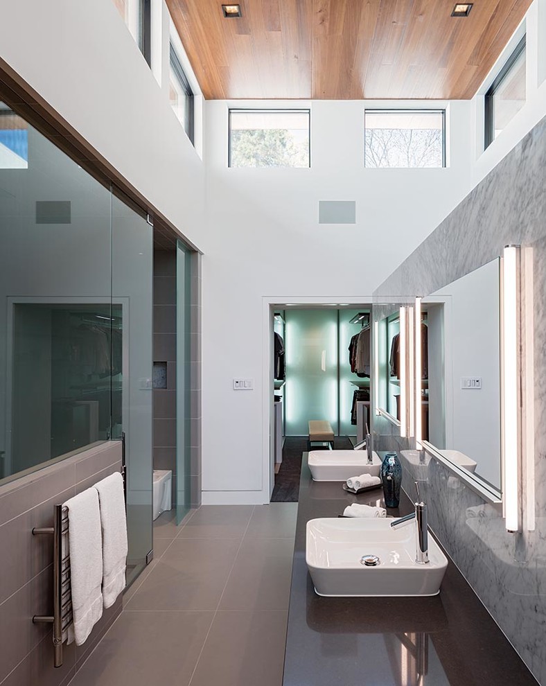 Design ideas for a large contemporary ensuite bathroom in Houston with flat-panel cabinets, medium wood cabinets, a wall mounted toilet, grey tiles, white walls, porcelain flooring, engineered stone worktops, a vessel sink and a built-in shower.
