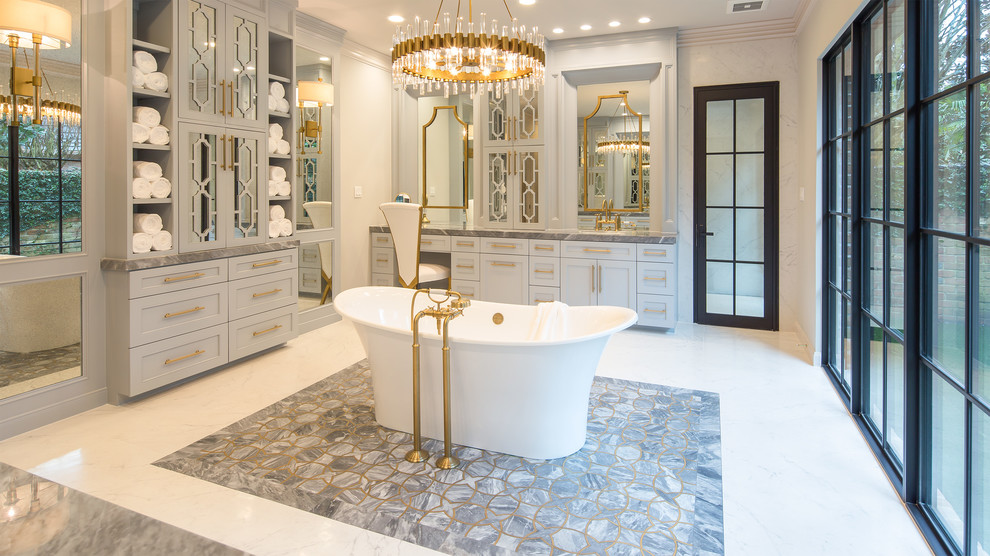 Inspiration for an expansive classic ensuite bathroom with freestanding cabinets, grey cabinets, a freestanding bath, a built-in shower, a wall mounted toilet, white tiles, porcelain tiles, white walls, porcelain flooring, a built-in sink, marble worktops, white floors and a hinged door.