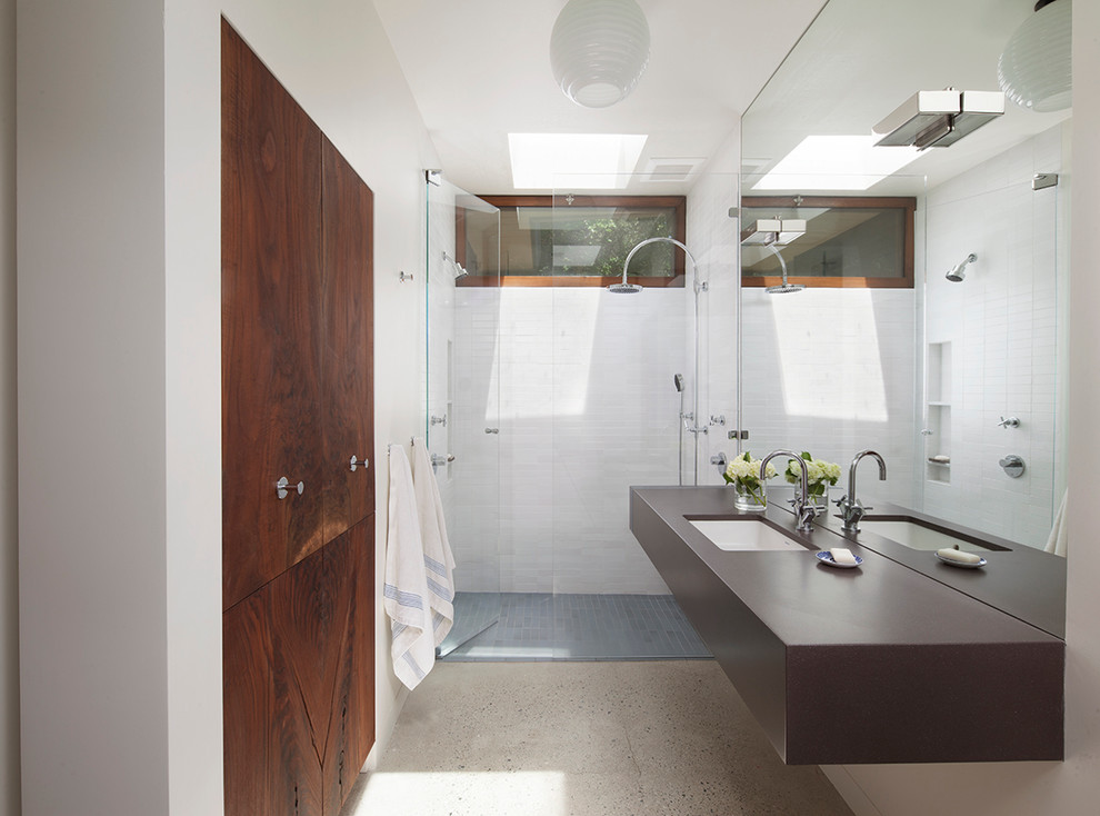 Foto på ett mellanstort funkis badrum med dusch, med ett undermonterad handfat, en dusch i en alkov, vit kakel, vita väggar, betonggolv och skåp i mörkt trä