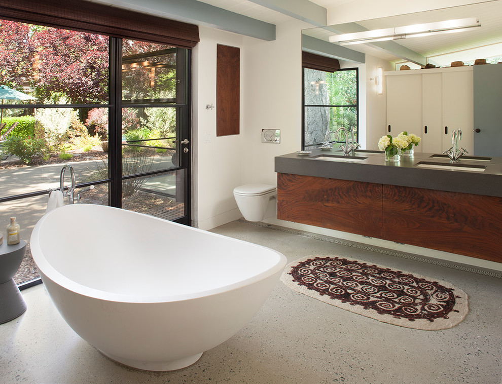 Réalisation d'une salle de bain principale design en bois foncé de taille moyenne avec un lavabo encastré, un placard à porte plane, une baignoire indépendante, WC suspendus, un mur blanc et sol en béton ciré.