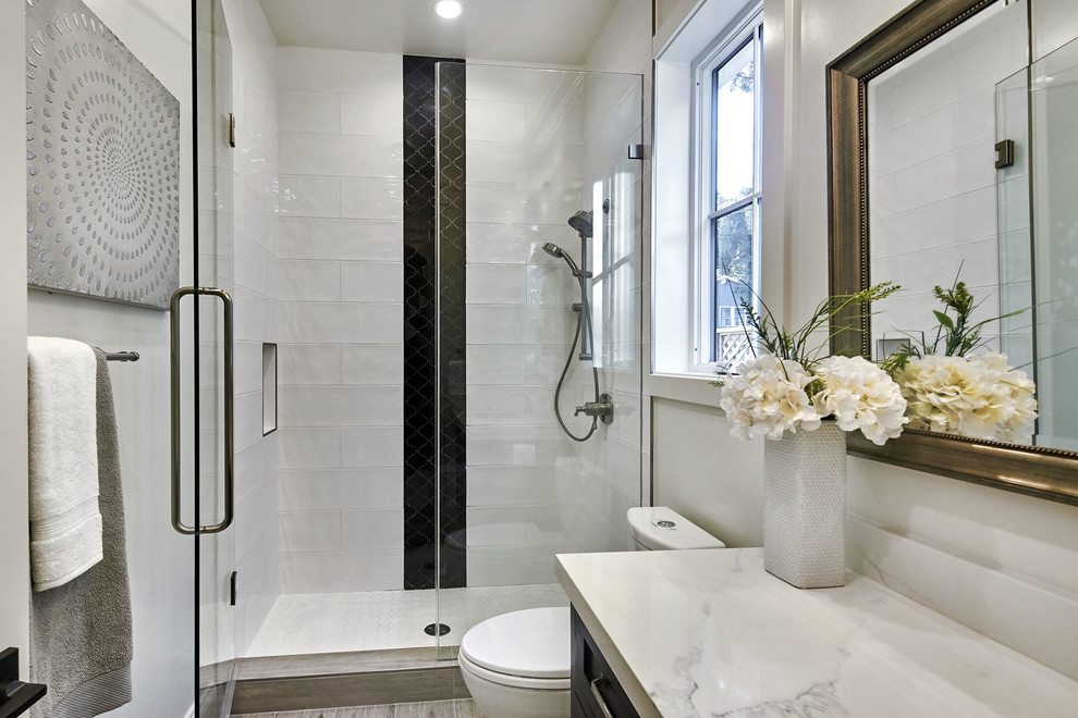 Idée de décoration pour une salle de bain champêtre de taille moyenne avec un placard à porte shaker, des portes de placard noires, WC à poser, un carrelage blanc, un carrelage métro, un mur blanc, un sol en carrelage de porcelaine, un lavabo encastré, un plan de toilette en quartz modifié, un sol gris, une cabine de douche à porte battante et un plan de toilette blanc.