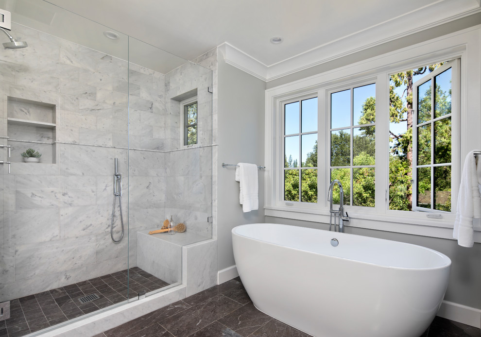 Photo of a large classic ensuite bathroom in San Francisco with recessed-panel cabinets, white cabinets, a freestanding bath, a corner shower, a one-piece toilet, white tiles, marble tiles, grey walls, slate flooring, a submerged sink, marble worktops, black floors, a hinged door and white worktops.