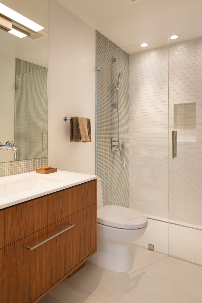Modern inredning av ett badrum, med släta luckor, skåp i mellenmörkt trä, en dusch i en alkov, en toalettstol med hel cisternkåpa, grå kakel, vit kakel, vita väggar, ett undermonterad handfat och dusch med gångjärnsdörr