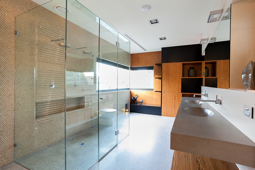 Modernes Badezimmer mit integriertem Waschbecken, flächenbündigen Schrankfronten, hellbraunen Holzschränken, bodengleicher Dusche, Toilette mit Aufsatzspülkasten, beigen Fliesen, Mosaikfliesen und weißer Wandfarbe in Melbourne